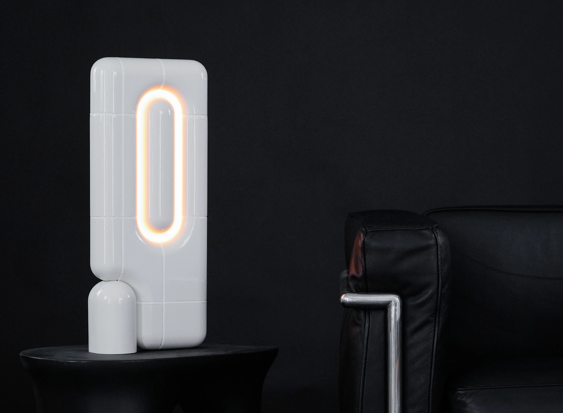 U·037 lamp in white high gloss on a black side table, beside a leather armchair