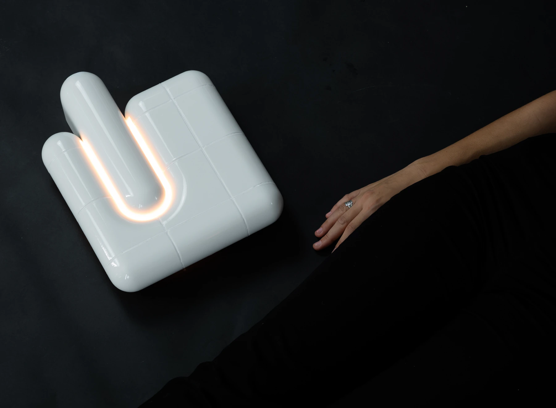 U·013 wall light in white high gloss, lit, with a hand reaching towards it